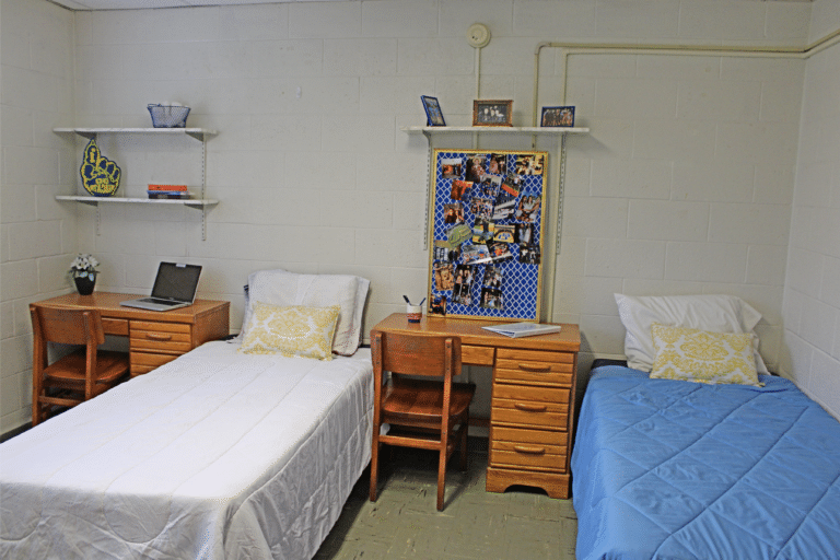 The inside of a double occupancy room inside of Merici Hall. There are two beds, two desks, and three shelves.